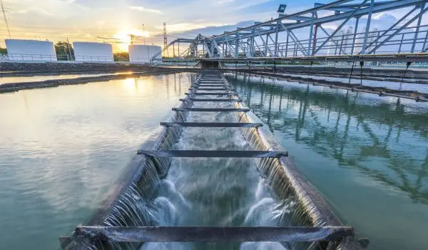 A water treatment plant with cascading flows and a structural metal framework against a backdrop of a setting sun and clear skies.