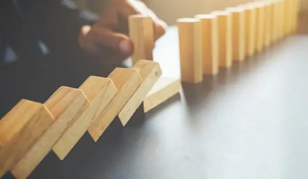 A hand is initiating a chain reaction by knocking over a row of standing wooden dominoes.
