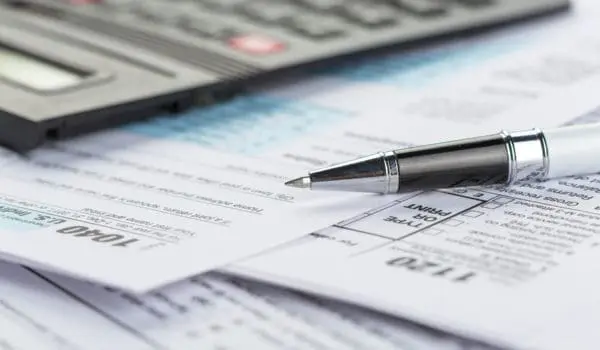 A pen and a calculator are placed on top of several tax forms.