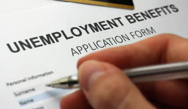 A person is filling out an unemployment benefits application form with a pen.