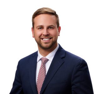 A man in a suit and tie is smiling against a white background.